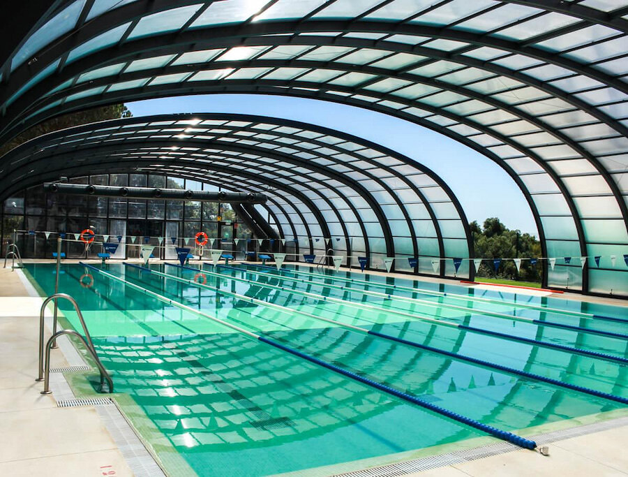 Indoor swimming pool at Sotogrande International School, featuring a sleek, curved glass roof that allows natural light to flood the space. The Olympic-style lanes and modern facilities highlight the school's commitment to sports and student well-being.