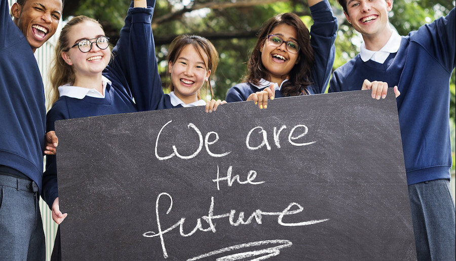 Group of diverse and cheerful students in school uniforms holding a large chalkboard sign that reads