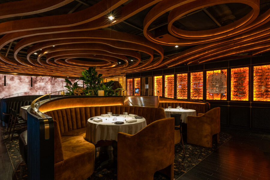 Elegante interior del restaurante Leña con diseño de techo de madera curvada, iluminación cálida y mesas de comedor redondas.