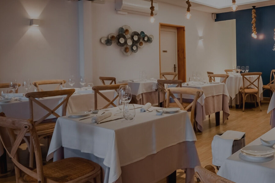 Interior de un elegante restaurante con mesas vestidas con manteles blancos, copas de vino y sillas de madera, en un ambiente acogedor y bien iluminado.